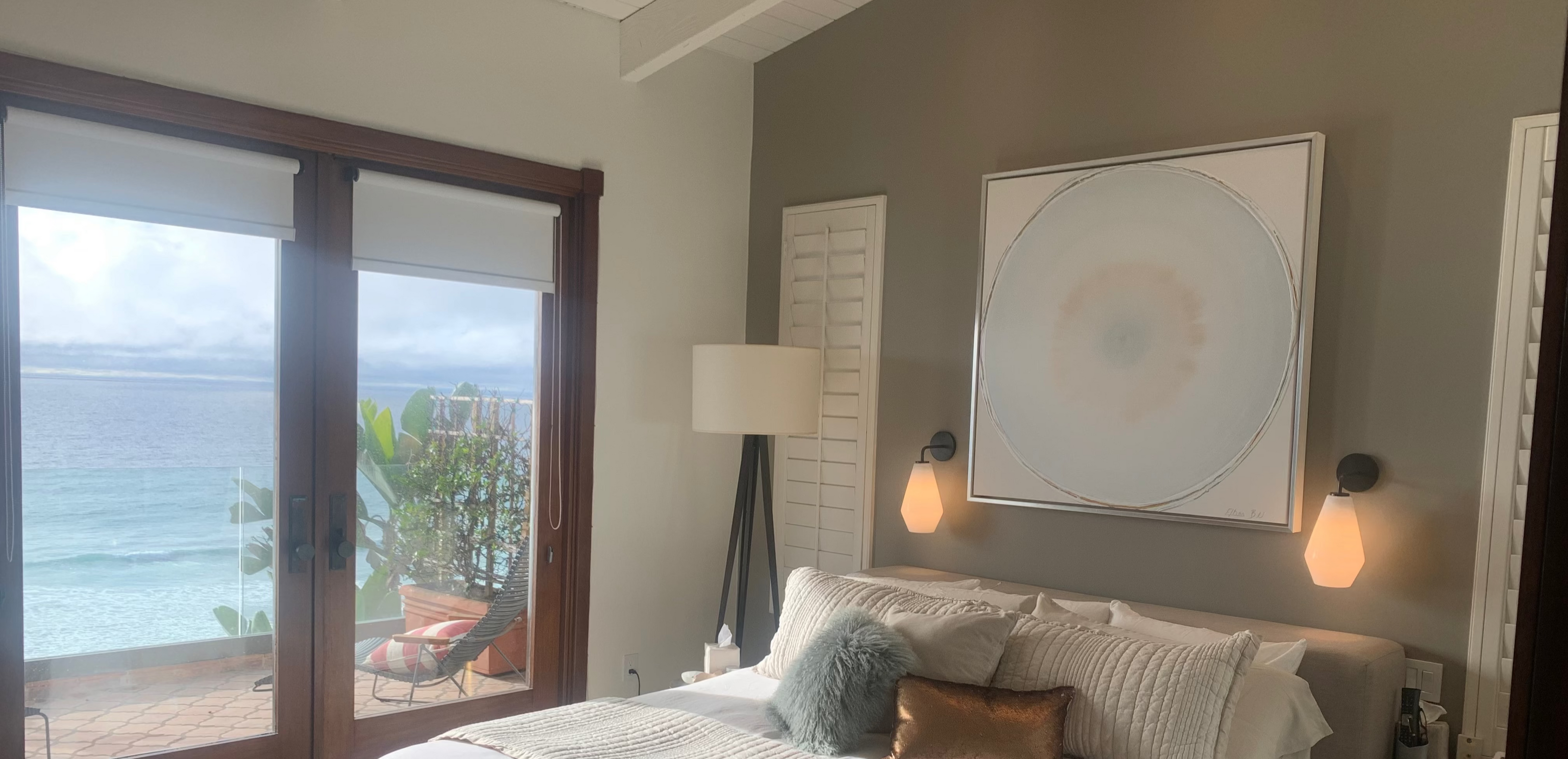 Modern bedroom with a large bed, artwork on the wall, and a view of the ocean through a glass door.
